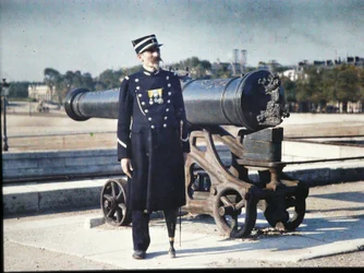 En soldat i uniform med tre medaljer står ved siden av en kanon i Paris, 1918 (autokrom)